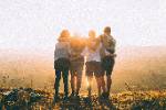 group of people with arms around each other on mountain top watching sunset